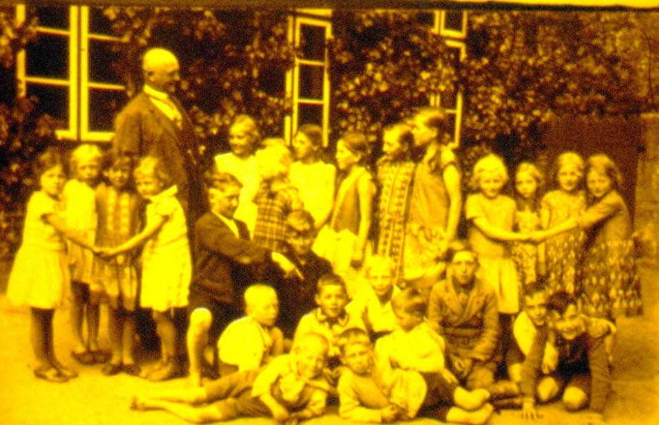 1924 Schulfoto Schmalensee: Das Bild zeigt eine gr��ere Gruppe von Sch�lerinnen und Sch�lern, die im Freien vor dem Schmalenseeer Schulgeb�ude posiert. Die Aufnahme stammt aus dem Jahr 1924 und ist in einem warmen, leicht vergilbten Ton gehalten. Die Kind